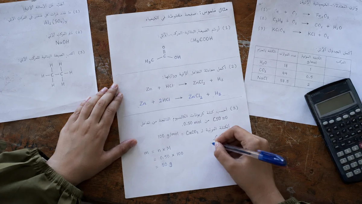 يدا طالبة تحلان صفحة كيمياء تجمع بنية مركب ومعادلة تفاعل ومسألة حسابية